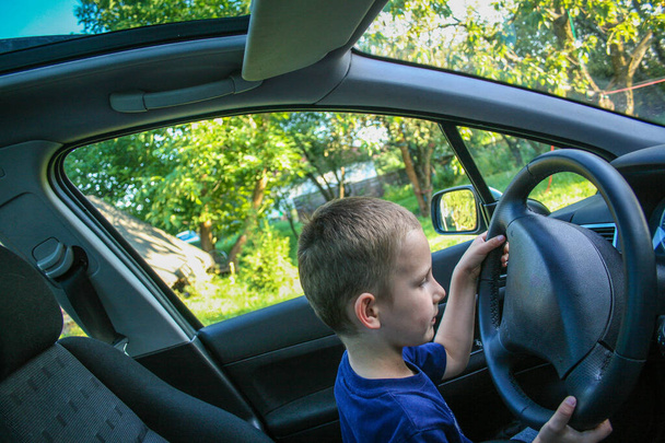 Τετράχρονο αγοράκι κάθεται πίσω από το τιμόνι και προσποιείται ότι οδηγεί. - Φωτογραφία, εικόνα