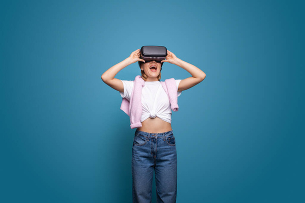 Caucasian woman in a VR glasses surprised with what she saw. She is touching with hands 3D glasses and express the emotions. Game, virtual reality. Blue - Φωτογραφία, εικόνα