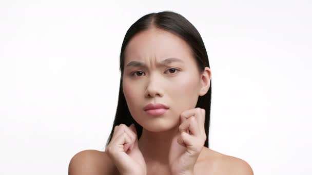 Elégedetlen ázsiai nő tapogató arc bőr fehér háttér - Felvétel, videó