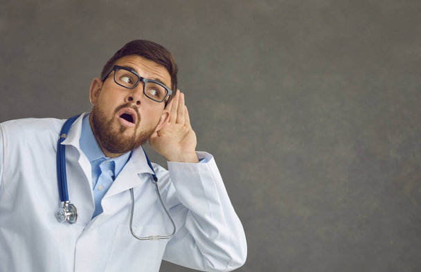 Funny curious doctor with hand at ear listening to colleagues sharing work gossips - Photo, Image