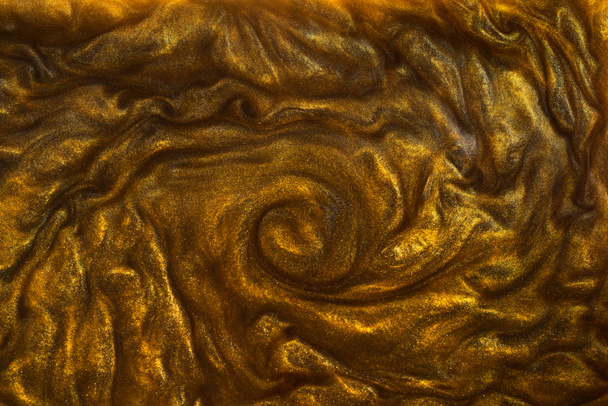 Die Textur von flüssigem Gold mit dem Zusatz von glänzendem Pigment. Abstrakte goldene Textur von Wellen, Wirbeln. Goldene flüssige Acrylfarben. Modernes Gestaltungselement.  - Foto, Bild