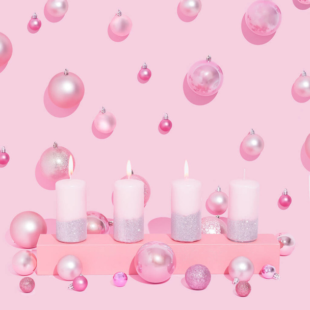 Рожеві пригоди Свічки поспіль на пастельному рожевому тлі. Різдвяні кульки. Третя свічка, освітлена, символізує радість
. - Фото, зображення