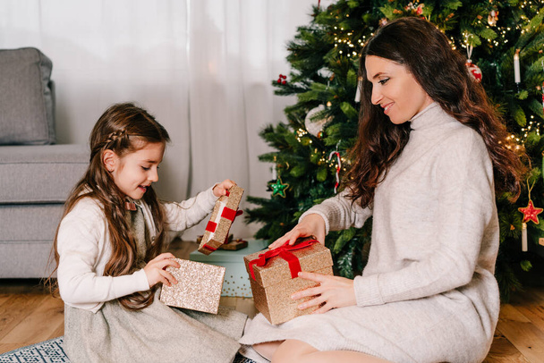 Excited mother and daughter sitting at home near beautiful decorated Christmas tree and enjoying opening their presents. Single solo parenting holidays. Family happiness. Selective focus - Foto, imagen