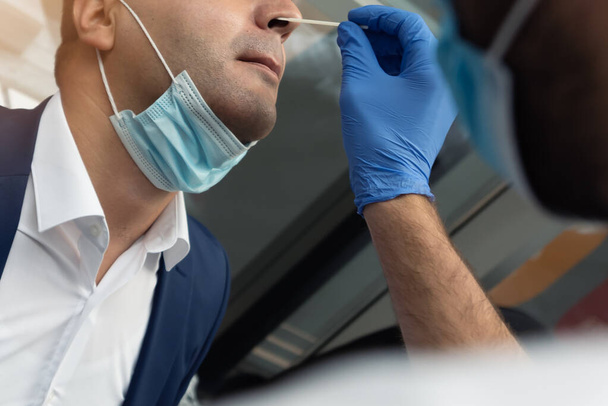 Nasale coronavirus PCR test. Dokter met behulp van wattenstaafje te nemen covid virus specimen van potentieel geïnfecteerde zakenman - Foto, afbeelding