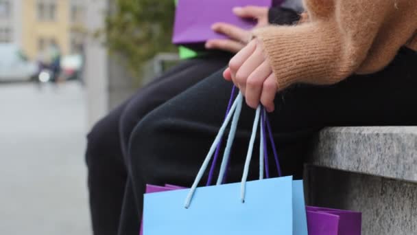 Neznámý dva lidé sedí na ulici ve městě ruce drží světlé nákupy tašky nerozpoznatelné zákazníky po nákupu slevy prodej na černý pátek venku close-up ženské nohy s černými kalhotami - Záběry, video
