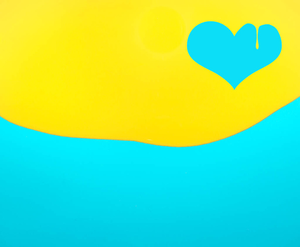 Símbolo en forma de corazón hecho de pintura amarilla goteando sobre fondo azul. Asiento plano, vista superior. Amor abstracto mínimo y concepto de San Valentín. - Foto, imagen