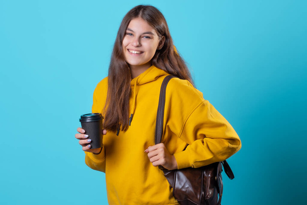 Cute young brunette in jeans and yellow hoodie. A beautiful student - 写真・画像