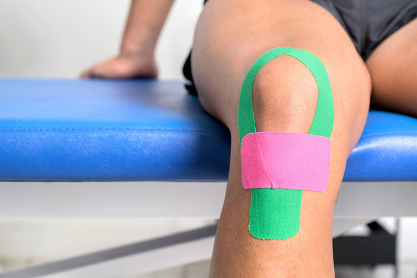 Young sportive male athlete treating injured knee with kinesio tape. Close up. Kinesiology, physical therapy, rehabilitation concept. - Foto, Imagem
