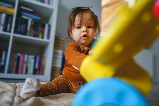 Un petit bébé caucasien de six ou sept mois jouant avec un jouet sur le sol à la maison dans la chambre seule bébé fille s'amusant à examiner un nouveau jouet grandissant de vraies personnes concept copier l'espace vue de face - Photo, image