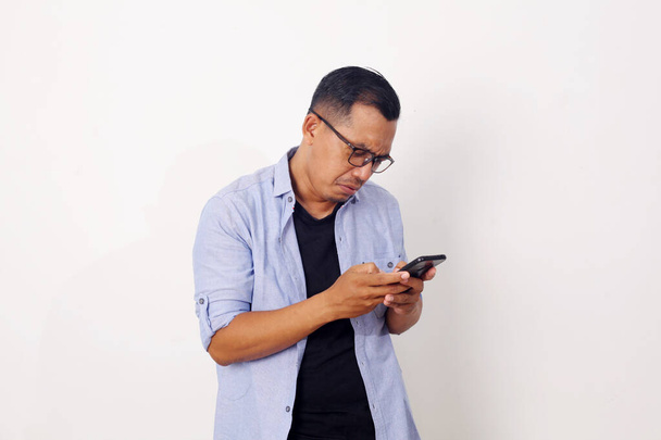 Attractive young Asian man reading texting chatting on his phone, bad news, sad crying expression - Photo, Image