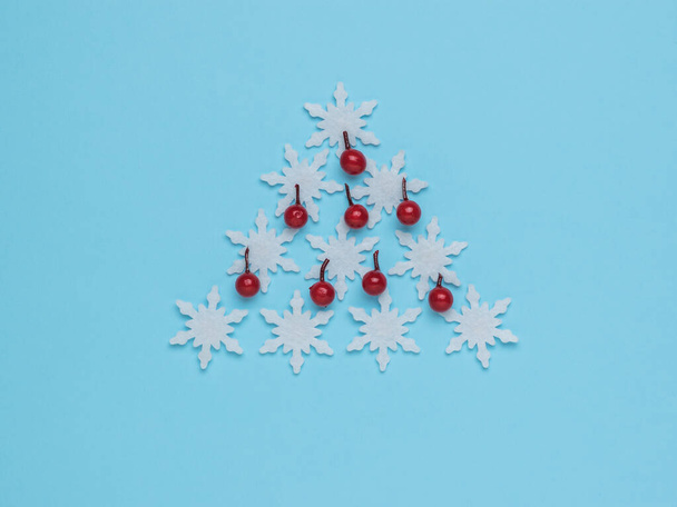 Árbol de Navidad hecho de copos de nieve blancos y bayas sobre un fondo azul. El concepto mínimo del Año Nuevo. Árbol de Navidad. Arte contemporáneo. - Foto, imagen