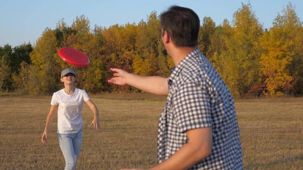 Мужчина и женщина играют, бросают друг другу красный диск в парке. Беззаботная пара, молодые люди веселятся вместе. Спорт и молодость. Счастливая семья играет в парке, дочь и отец - Фото, изображение