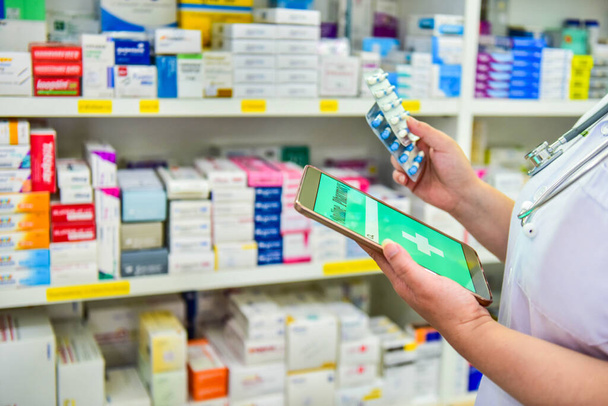 Farmacia segurando cápsula pack e touch pad para barra de pesquisa em exposição em farmácia prateleiras farmácia fundo. Conceito médico online. - Foto, Imagem