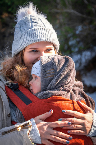 Portrait of beautiful caucasian babywearing mother with her son in baby carrier winter outdoor. - Foto, imagen