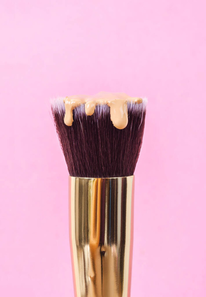 pouring liquid beige makeup foundation on a brush makeup with pink background. - Фото, зображення