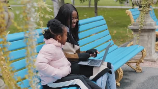 Щаслива афро-американська сім'я використовує ноутбук молода мати з маленькою донькою спілкується сидячи на вулиці, мама посміхається вказівним пальцем на екрані милий малюк і афромама робить відео виклик комп'ютерній програмі - Кадри, відео