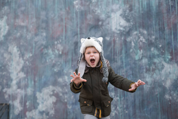 The roar of a wolf. Child in a wolf hat on gray background, outdoor. High quality photo - Fotó, kép