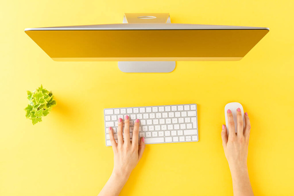 Female hands using modern computer with accessories on yellow background. Office desktop. Top view - 写真・画像