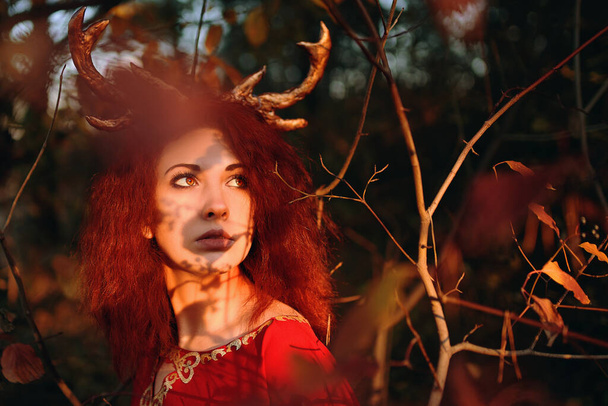 Mujer en vestido rojo largo con cuernos de ciervo en el bosque de otoño. - Foto, Imagen