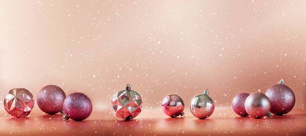 Pink and purple Christmas tree balls on pinkish orange coral background with falling snow - Фото, изображение