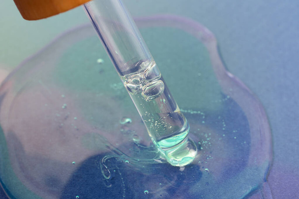 Macro fotografia della pipetta di vetro nel gel cosmetico liquido, colore blu. - Foto, immagini