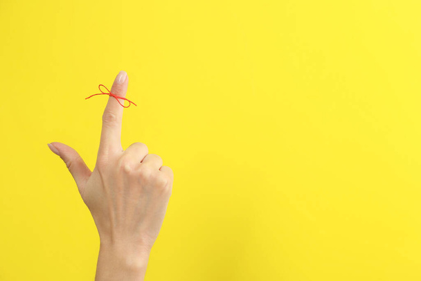 Woman showing index finger with tied red bow as reminder on yellow background, closeup. Space for text - Zdjęcie, obraz