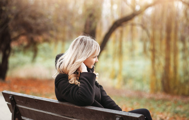 Young girl sitting on a bench in park on a fall day - Foto, imagen