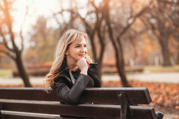 Jovem sentada em um banco no parque em um dia de outono
 - Foto, Imagem
