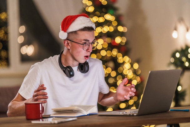 surprised teenager wearing headphones uses a laptop to prepare and take the college exam. a young man studies remotely at Christmas. sudden joy. E-Education Is Distance Home Education. Won a prize - Foto, immagini