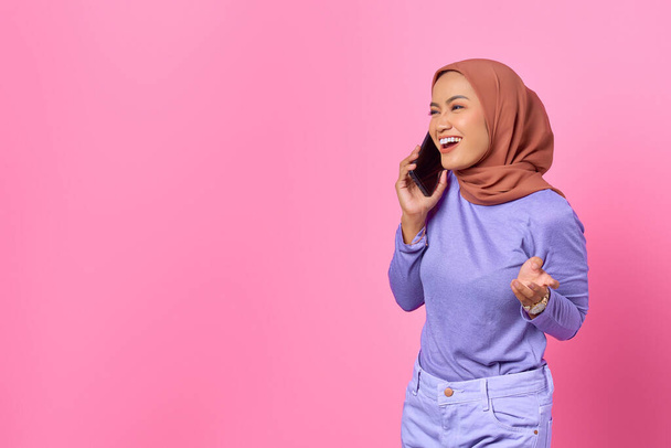 Portrait of smiling young Asian woman talking on a mobile phone on pink background - Photo, Image