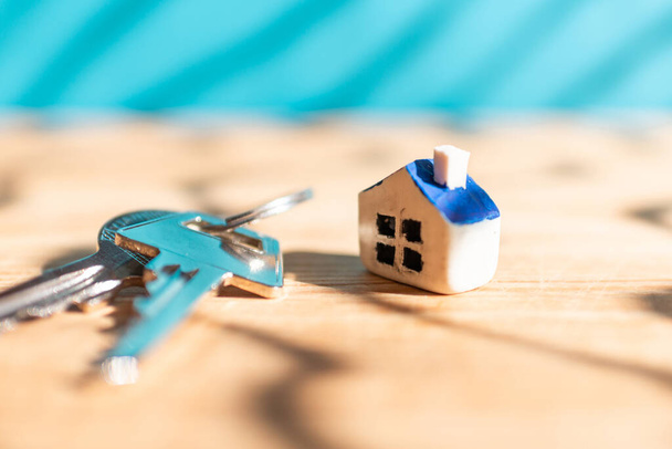 Casa nuova in miniatura con chiavi di casa su sfondo sfocato blu legno, immobiliare e concetto di business immobiliare. Primo piano, messa a fuoco selettiva. - Foto, immagini