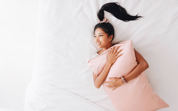 Beautiful Indonesian girl lying on a pink pillow with a silk pillowcase. View from abov - Photo, Image