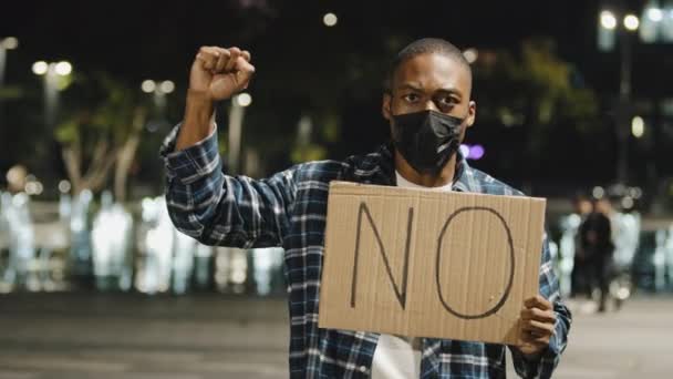医療マスクのアフリカ系アメリカ人男性は夜市の看板バナーを保持立っている段ボールテキストいいえ、怒り男抗議の叫びを振って抗議活動の不一致否定黒の生活問題 - 映像、動画