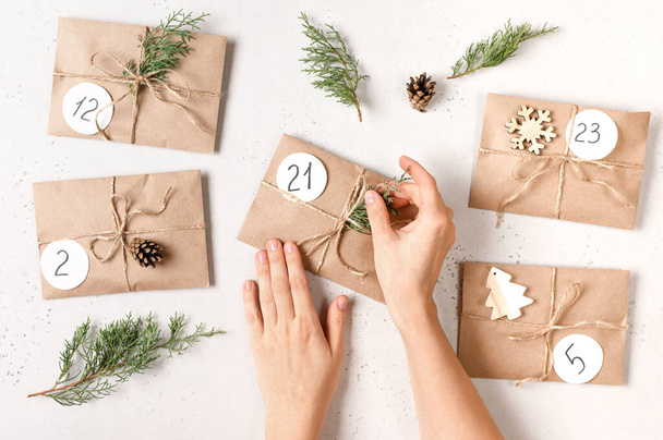Christmas advent calendar. Female hands making gifts with kraft envelopes, fir branches, pine cones. Top view. - Foto, Bild