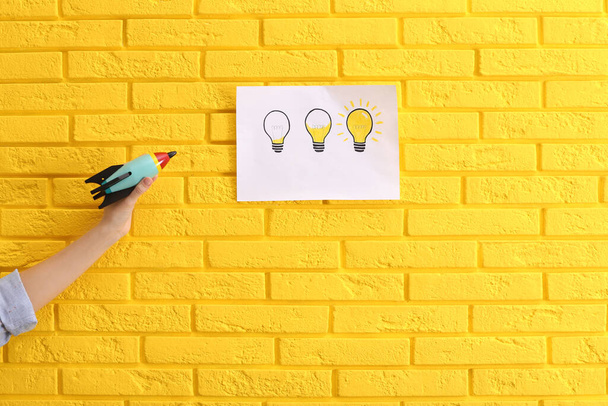 Woman holding toy rocket near yellow brick wall with lamps drawing, closeup. Startup concept - Foto, Bild