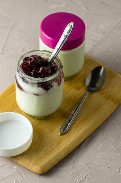 a jar of yogurt with cherry jam on a cutting board next to other jars of yogurt. High quality photo - Fotoğraf, Görsel