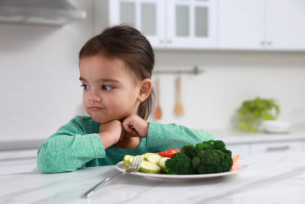 Cute little girl refusing to eat vegetables in kitchen - Foto, Imagen