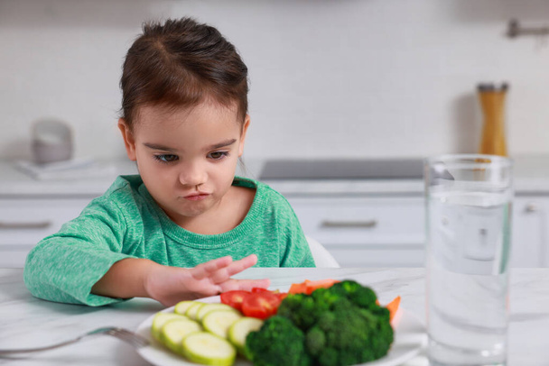 Cute little girl refusing to eat vegetables in kitchen - Fotoğraf, Görsel
