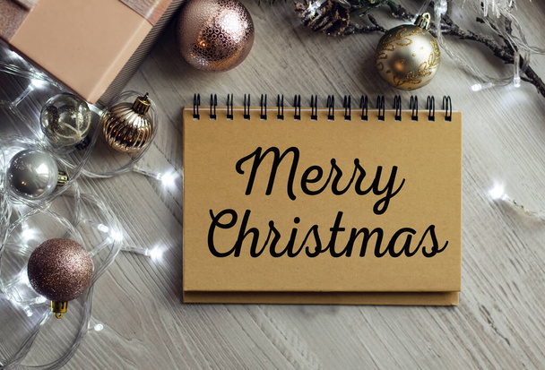 Notepad on the table with the text MERRY CHRISTMAS. Christmas background with decorations from balls and garlands. Delicate shades. Christmas or festive concept. - Photo, image