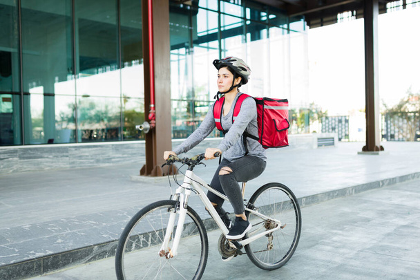 Приваблива молода жінка катається на велосипеді з шоломом і працює як дівчина з доставки для мобільного додатку
 - Фото, зображення