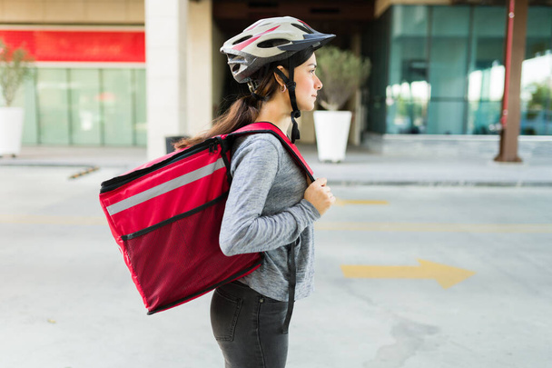 Profiel van een latijn jonge vrouw met een levering rugzak met voedsel krijgen van haar fiets in de stad - Foto, afbeelding