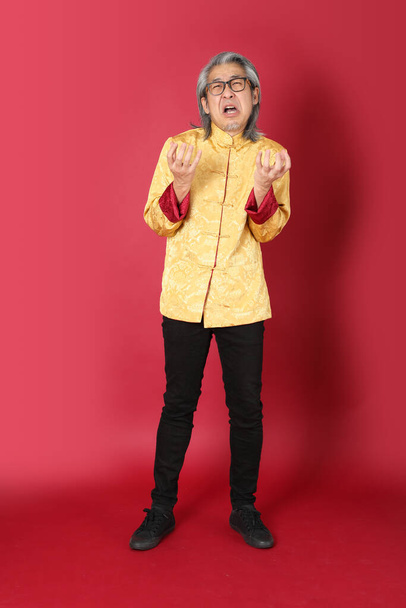 The senior Asian man wearing traditional gold chinese dresses standing on the red background. - Fotografie, Obrázek