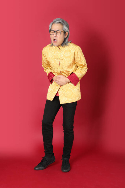 The senior Asian man wearing traditional gold chinese dresses standing on the red background. - Foto, immagini