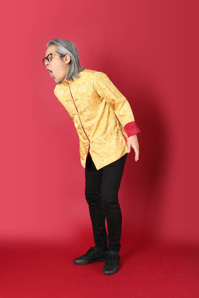 The senior Asian man wearing traditional gold chinese dresses standing on the red background. - Φωτογραφία, εικόνα