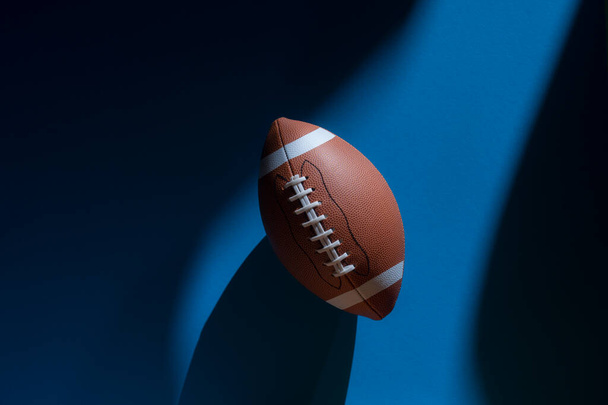 American Football Ball mit natürlicher Beleuchtung auf blauem Hintergrund. Horizontales Sport-Themenposter, Grußkarten, Kopfzeilen, Website und App - Foto, Bild