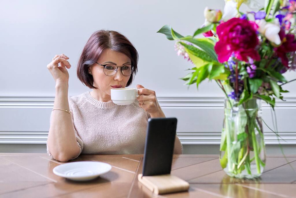 Middle-aged woman sitting at home using a smartphone for relaxation - Photo, image