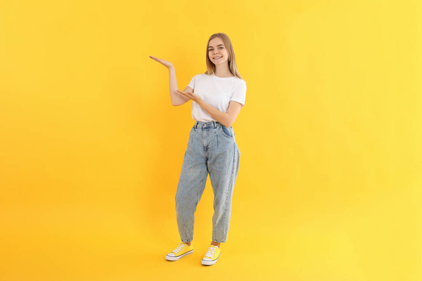 Young attractive girl in jeans on yellow background - Foto, Imagen