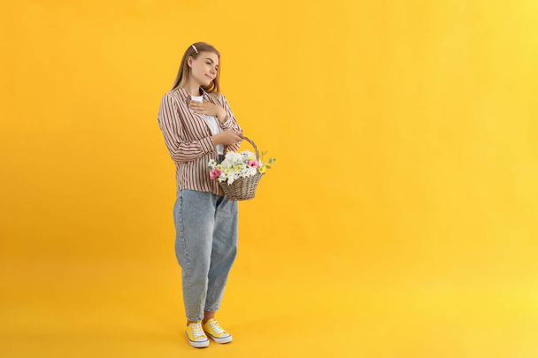 Attractive girl with basket of flowers on yellow background - Zdjęcie, obraz