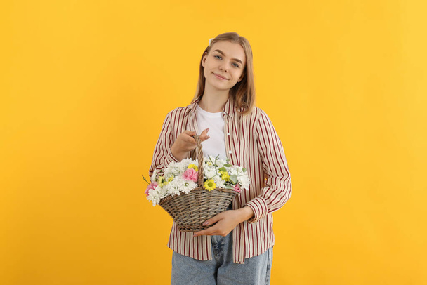 Attractive girl with basket of flowers on yellow background - Valokuva, kuva