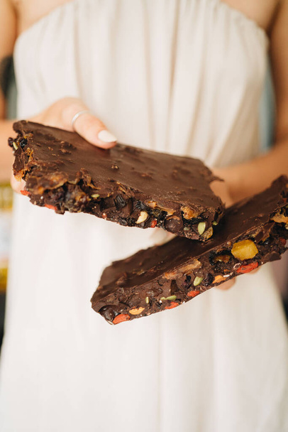 Woman is holding big piece of chocolate bar with nuts and dried fruits - Foto, immagini